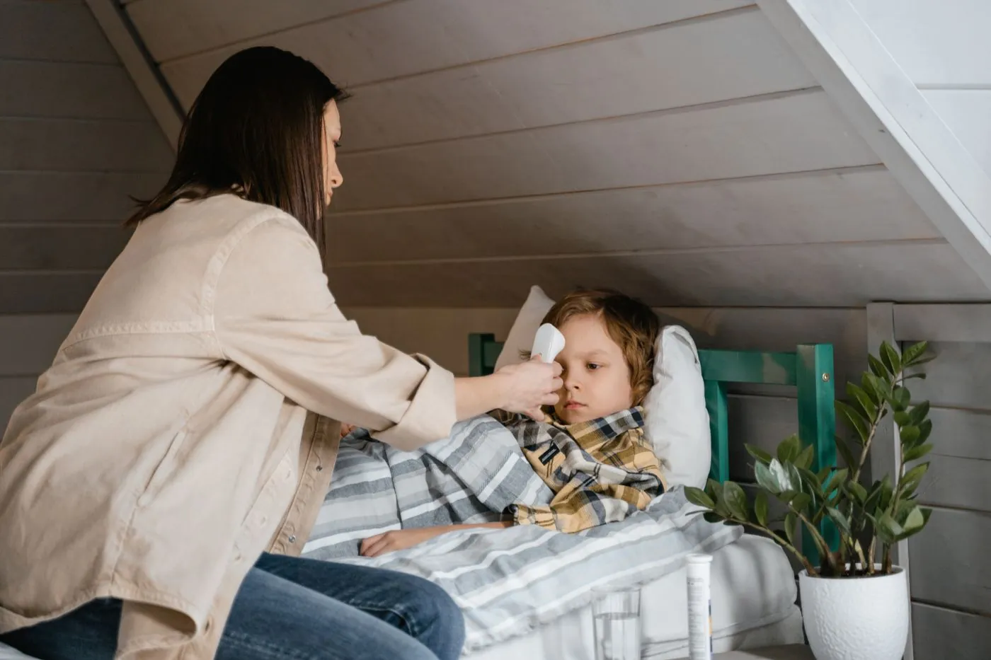 Maminka měří synovi teplotu, který leží nemocný v posteli