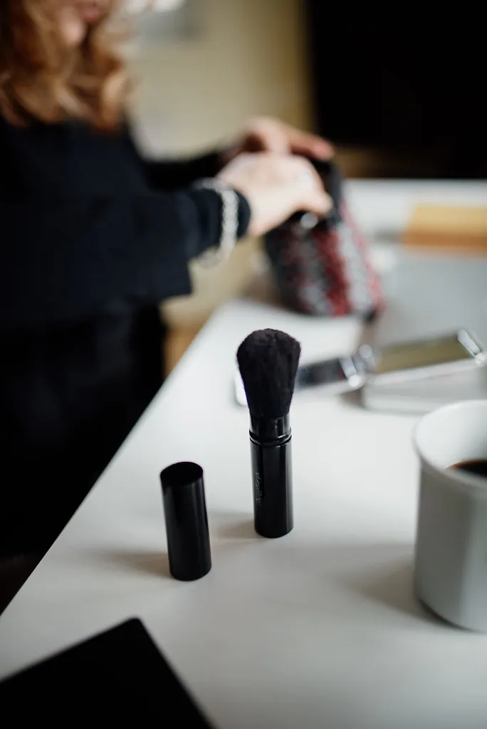 Žena si nanáší make-up štětcem u stolu s kosmetikou