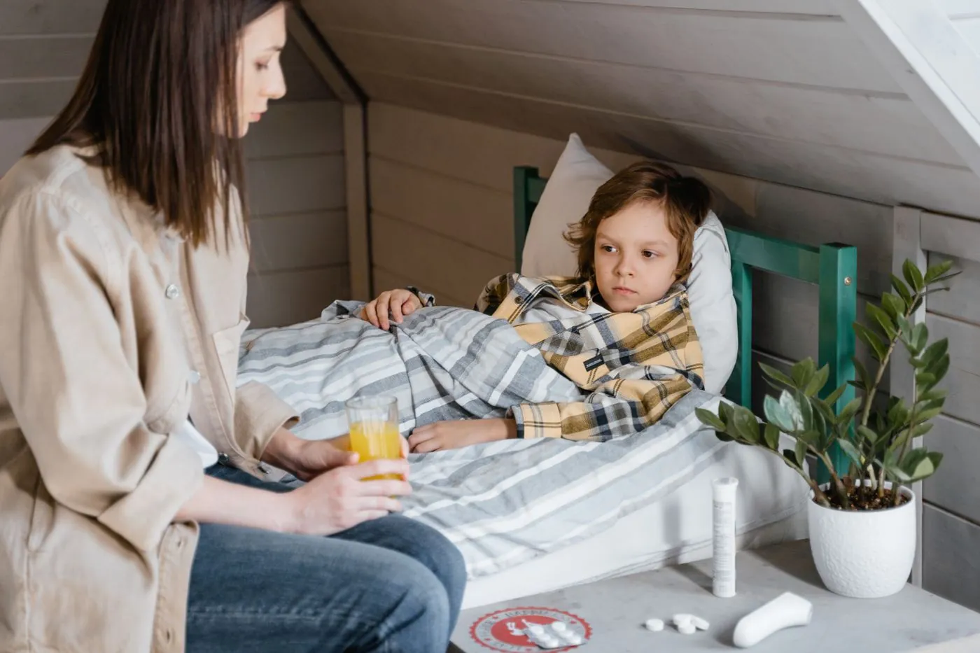 Maminka podává nemocnému dítěti pití na lůžku