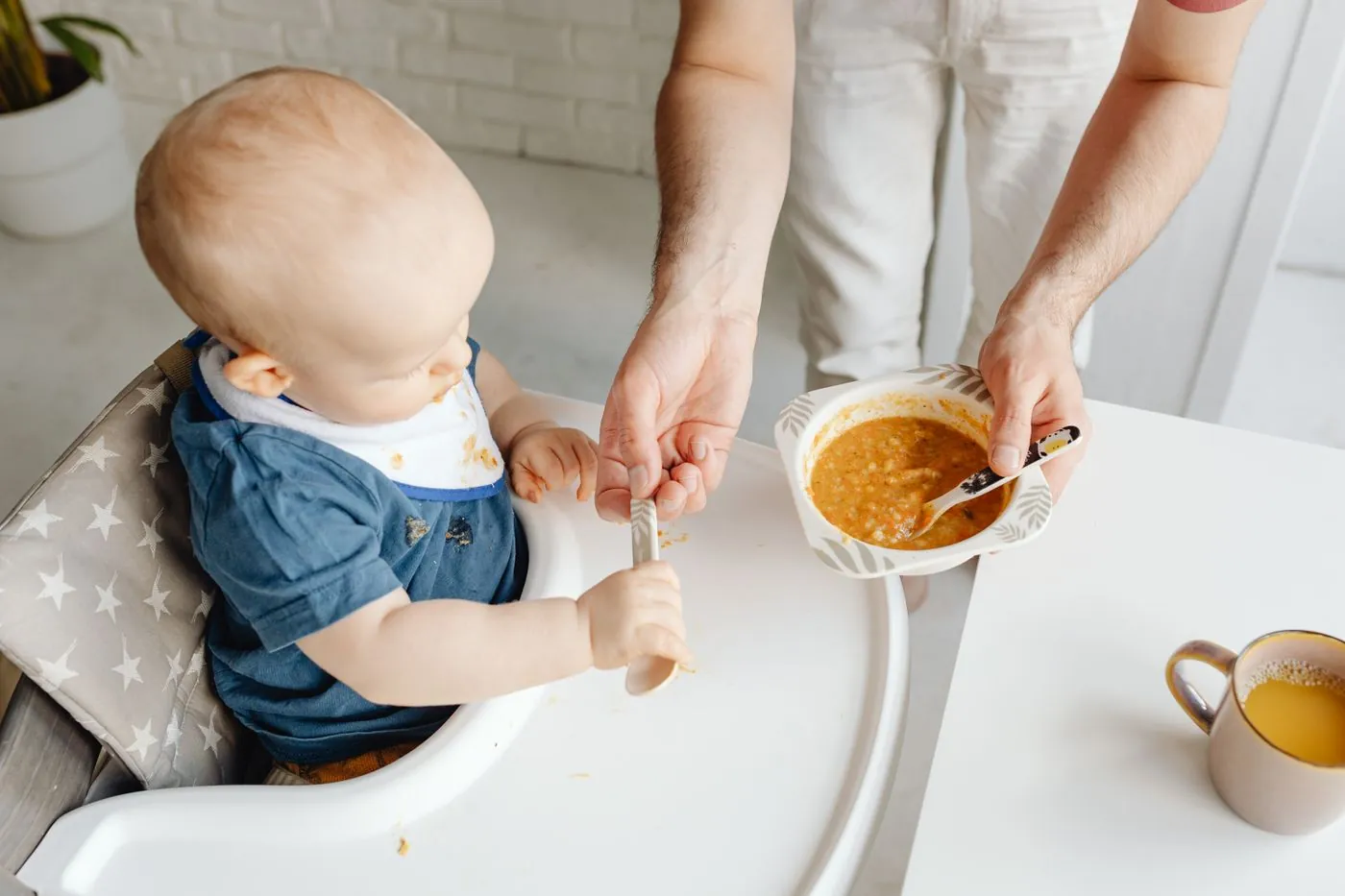 Miminko sedí v jídelní židličce a je krmeno kaší