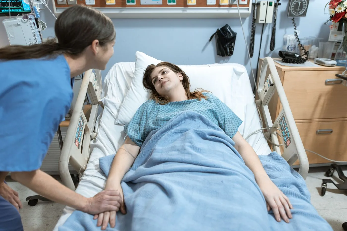 Zdravotní sestra drží ruku pacientky na lůžku v porodnici