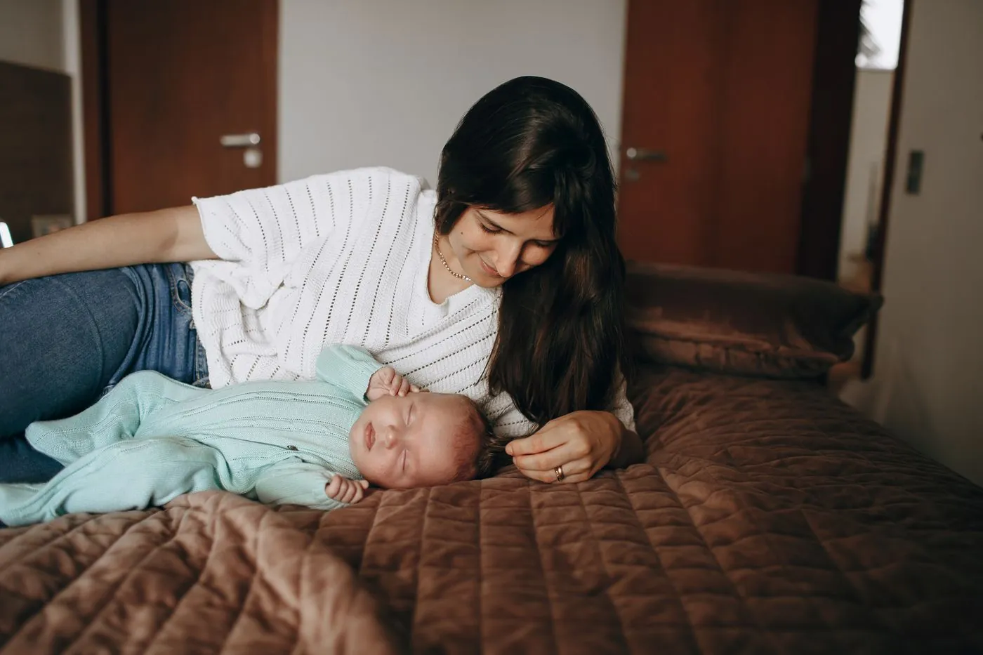 Maminka leží na posteli a láskyplně chová novorozence