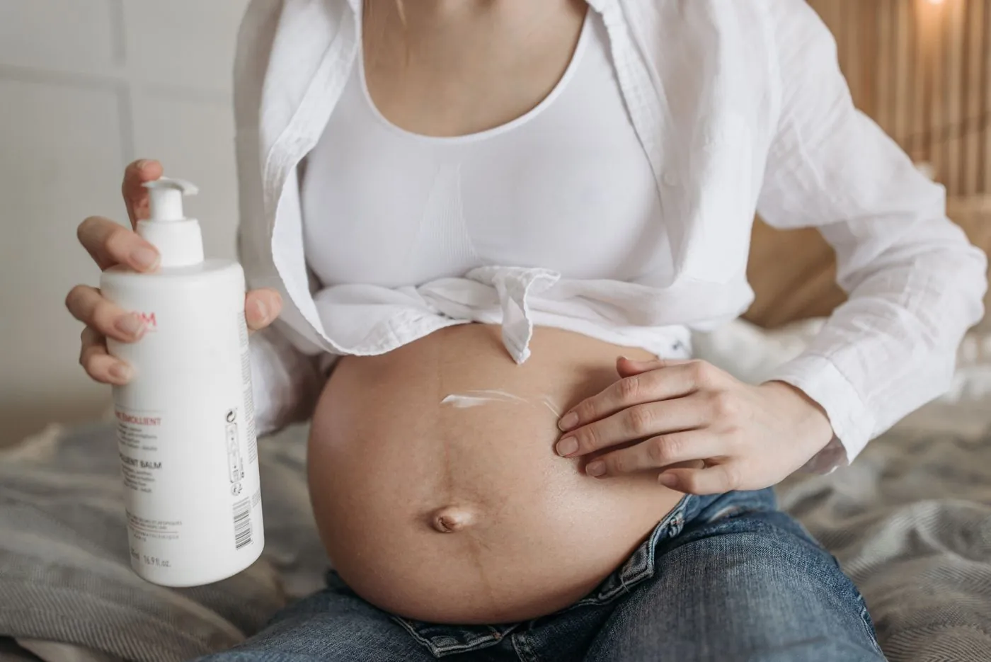 Těhotná žena si vmasírovává tělové mléko do bříška