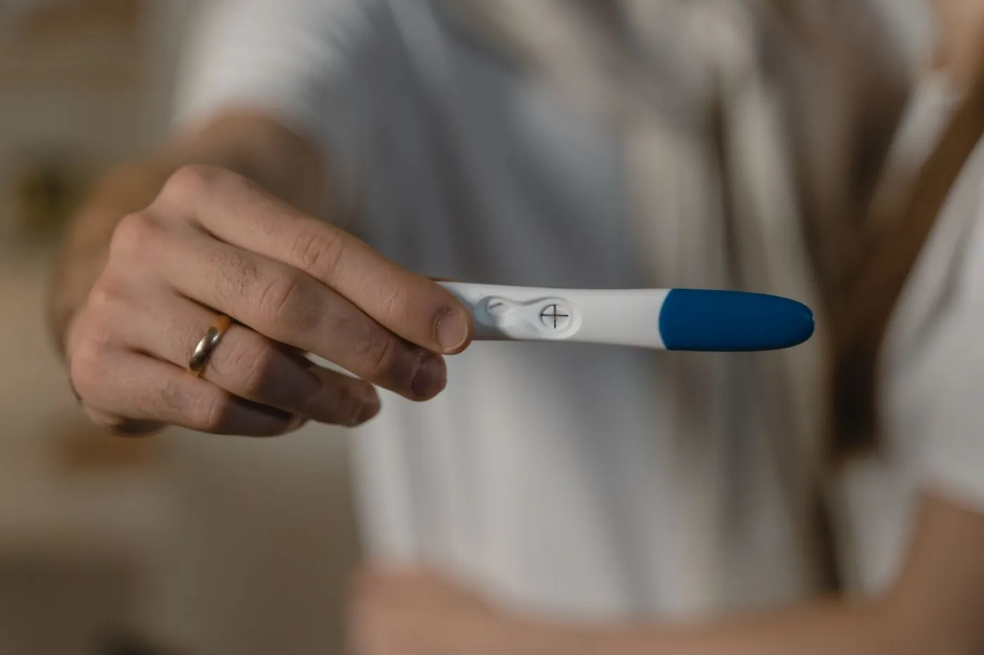 Ruka drží těhotenský test s modrým víčkem na krytu